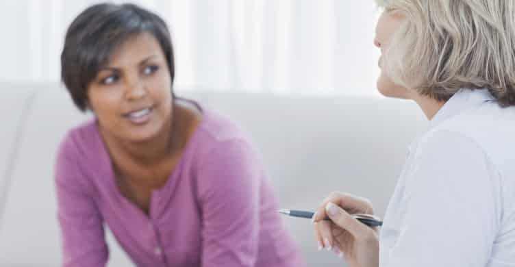 Therapist advising her smiling patient on couch in office